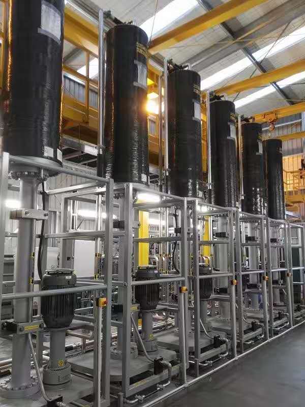 Industrial processing plant with tall black vertical tanks and stainless steel piping, pumps, and platforms.