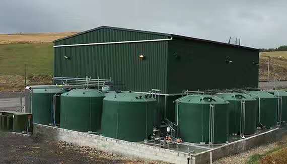 Green metal utility shed with several large green water tanks in front, on a concrete base in a rural area